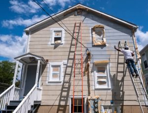 Painter on a ladder spraying paint on the exterior of a house